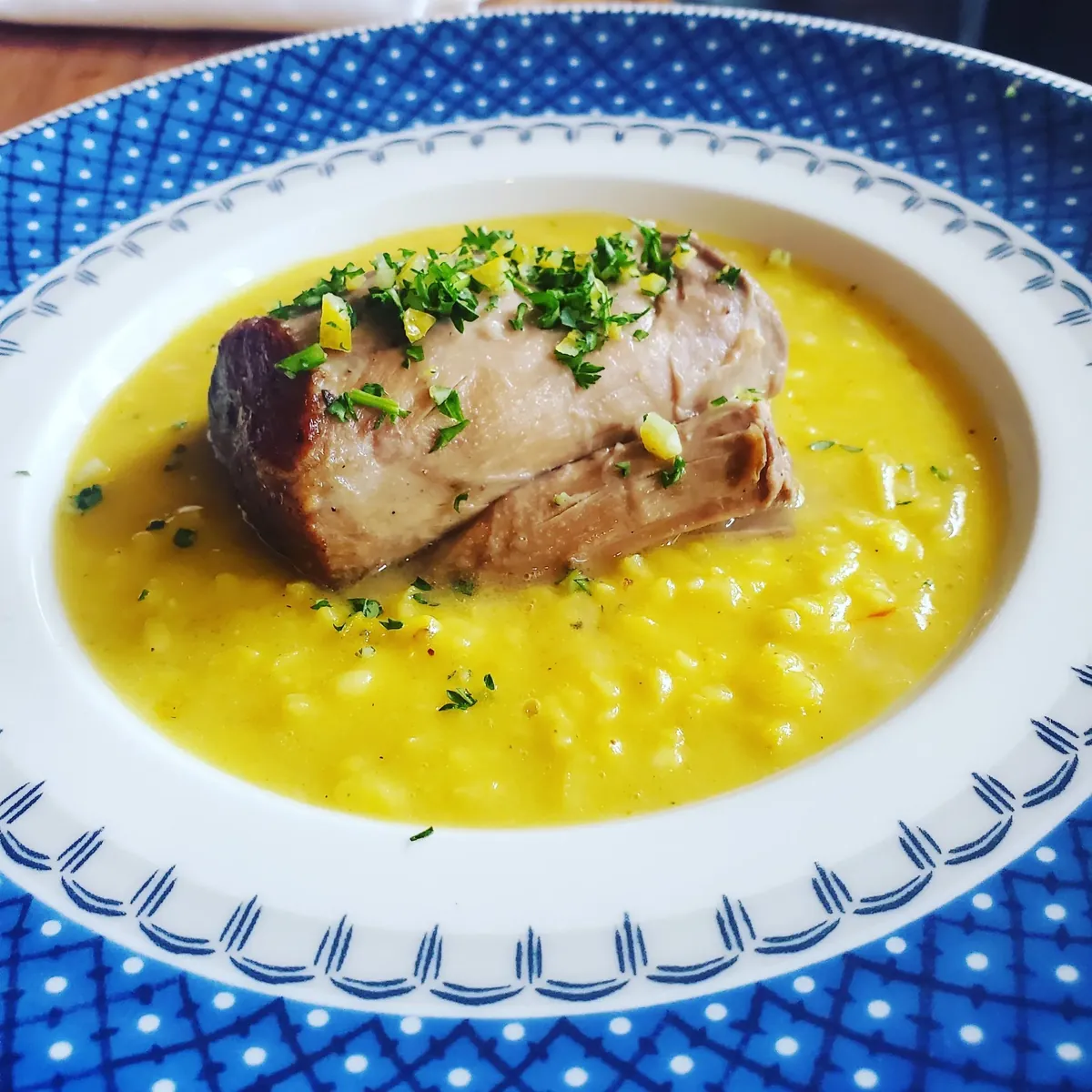 Seared fish over yellow sauce on a blue-rimmed plate